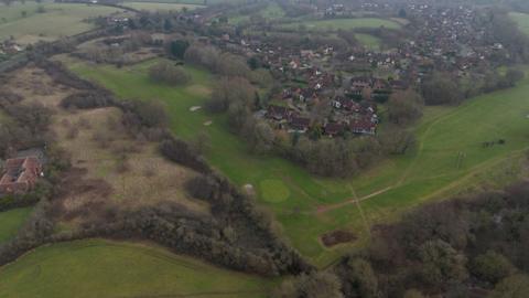 An aerial photography shows the area of the Abbey golf course that would be developed, as well as partially-wooded scrubland to the west. The existing Hither Green Lane estate is visible. 