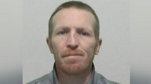 A headshot of a man with a ginger beard and wearing a grey jacket.