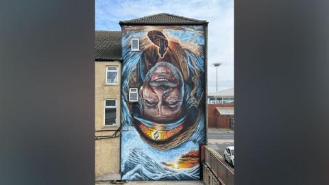 An upside down painting of a fisherman surrounded by swirling sea