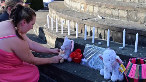 Two women leave a teddy and candles for the mum and daughter 