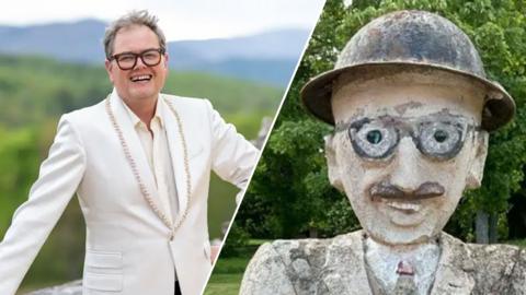Alan Carr, wearing dark glasses and a white blazer, and a cement statue of a man in a bowler hat and round glasses