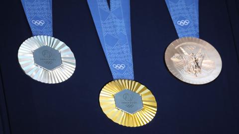 Olympic medals are displayed during the unveiling of the Paris 2024 Olympic and Paralympic Games Medals.

Silver, gold and bronze medallions hand on a blue ribbon