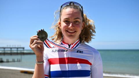 Zoe Backstedt in a British champion's jersey holds her gold medal on the sea-front at Aberystwyth