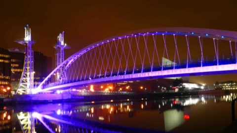 The Lowry Bridge at Salford Quays lit up in purple in the evening.