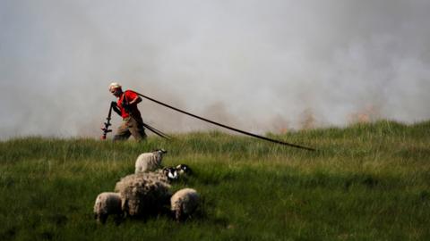 A firefighter carries a hose close to scorched moorland during a moorland fire at Winter Hill, near Rivington, July 2018.