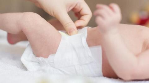 A baby is lying on its back on a white blanket getting its nappy changed by an adult.