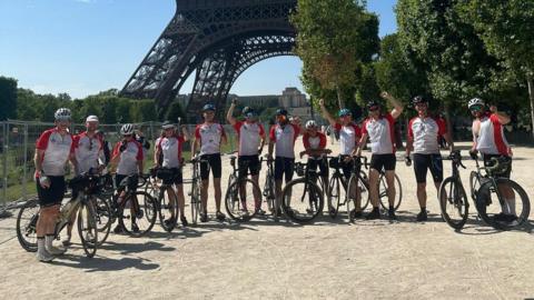A group of cyclists stand under the Eiffel Tower in Paris. 