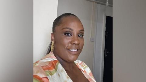 A selfie of Dionne. She is wearing an orange and green blouse and is smiling at the camera.