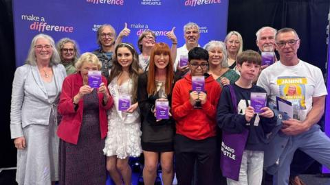 BBC Radio Newcastle's Make a Difference awards ceremony. The winners stand in front of purple signage that reads 'MAKE A DIFFERENCE' with the BBC Radio Newcastle branding.