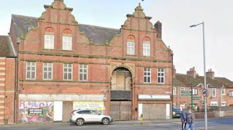Google Street view of The Arcade viewed from North Street. The building has ornate brickwork at the top, with the ground floor being largely boarded up.