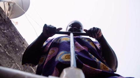 A woman stands above a borehole pump.