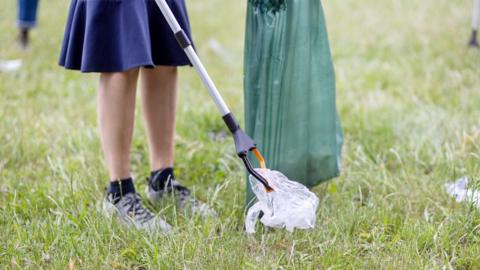 Cropped shot of woman volunteer collecting trash using tong and garbage bag in park