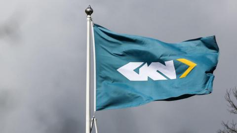 A teal flag on a white pole with the letters GKN in white lettering