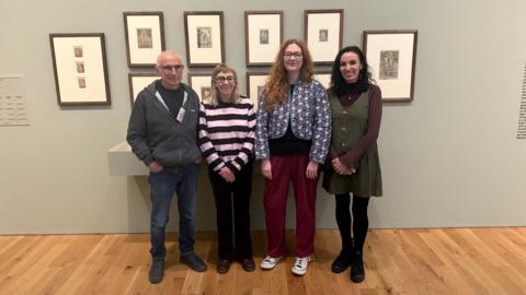 Pobl yn sefyll o flaen casgliad o luniau