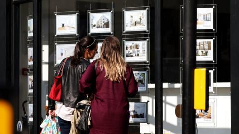 Two women look at houses in an estate agent's window