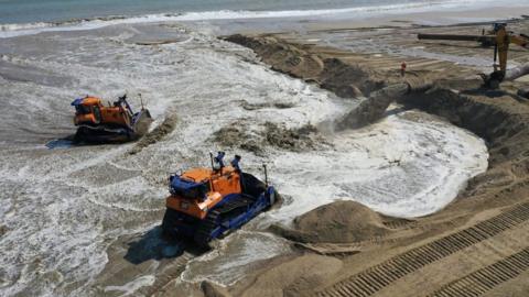 Bulldozers move sand on beach