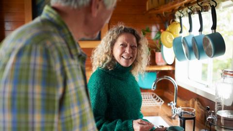 A mature woman smiling at her husband and making coffee in an eco lodge - stock photo