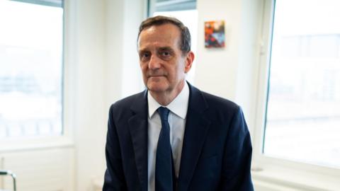 Stephen Parkinson in a suit tie in a brightly lit, white walled office