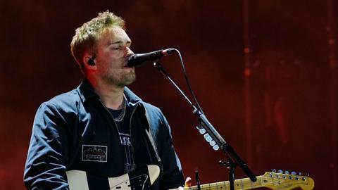 Sam Fender performing at Big Weekend, singing into a microphone while playing the guitar.