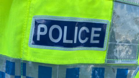 A generic image of the back of a high-vis yellow police jacket, with blue and grey checks and the lettering POLICE in capitals.