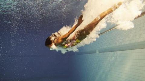 A generic underwater shot of a woman diving into a pool with a splash of water around them.