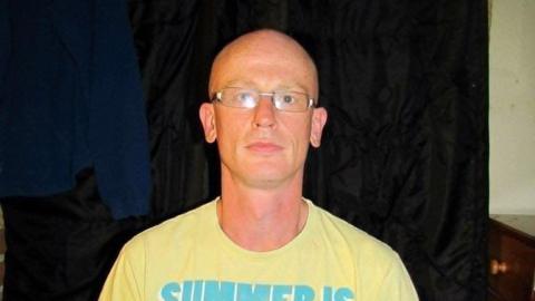 A head-and-shoulders picture of Stuart Caldicott. He has a shaven head and is wearing a yellow T-shirt and glasses.
