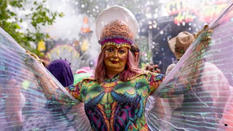 A woman dressed as a fairy with a gold face and an exposed brain with a glass dome over the top