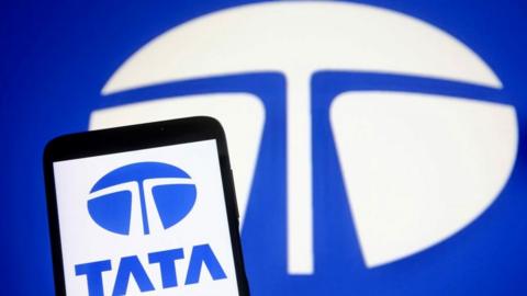 In this photo illustration, a Tata Group logo is seen on a smartphone and a pc screen