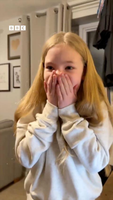 A young girl with blonde hair, wearing a white jumper.