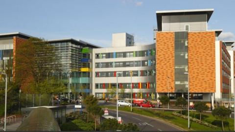 Curved front of hospital building with green, blue, red and yellow detailing to windows and road layout in front