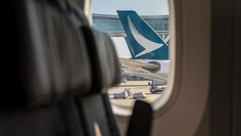 A view from inside an airplane cabin shows the tail of a Cathay Pacific plane at Hong Kong International Airport