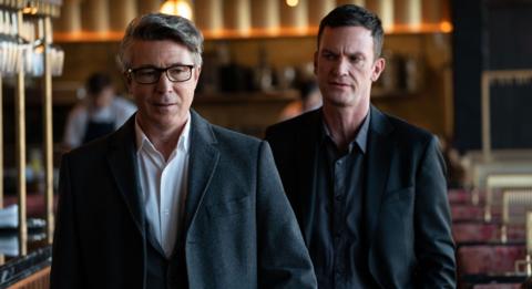 Two men walking through a bar / restaurant together. They look like they're having a tense conversation