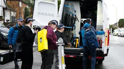 Police officers pack up outside a van on an urban street. 