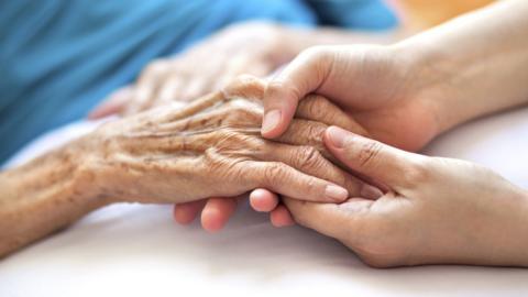 Woman holding senior woman"s hand on bed