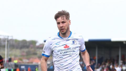 Sam Foley chasing after a ball at Holker Street with his light brown hair sticking up in the wind 