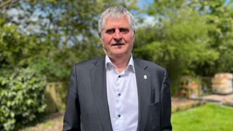 Deputy Rob Prow, he is standing in a garden wearing a suit 