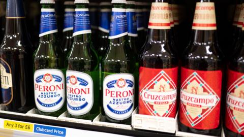 Bottles of beer on a supermarket shelf. In the bottom left corner is a label saying Any 3 for £6 Clubcard Price.