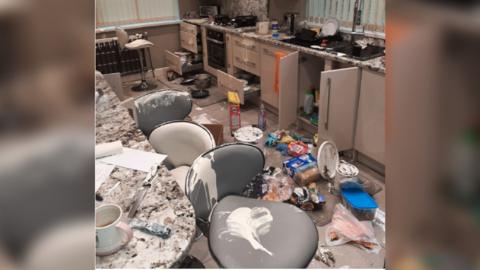 A kitchen has been ransacked, with mess all over the floor and white paint smeared over chairs