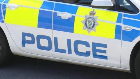 A close-up of the side of a police car, which is coloured white with blue and yellow panels, a Lincolnshire Police logo and the word "police" written in large capital letters.