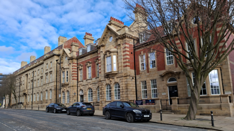A large building on a city street with cars parkd outside. 