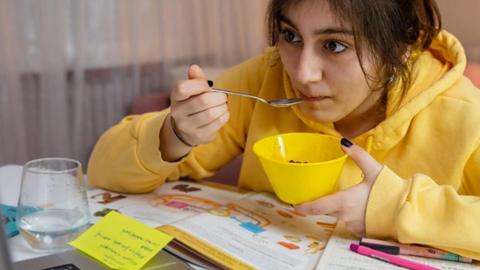 A young woman revises while eating a bowl of food