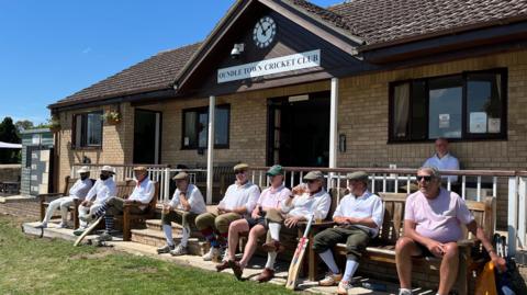 People sat on benches outside Oundle Town Cricket Club's clubhouse