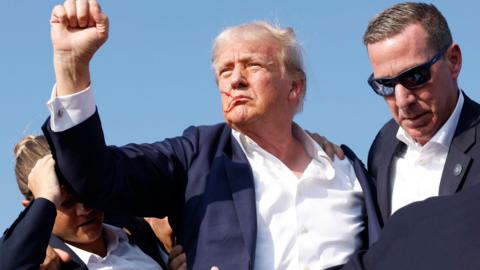 Donald Trump with blood on his face holding up his fist to crowd after an assassination attempt