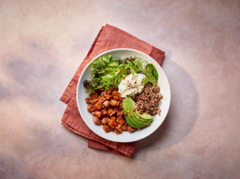 A white plate sitting on a napkin with hot honey beef, sweet potato, avocado, cottage cheese and spinach on it