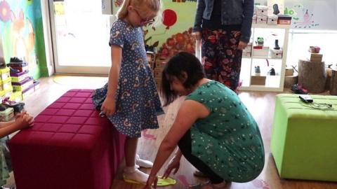 A member of staff helping Lydia try on shoes