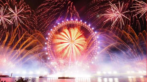 Orange and red fireworks exploding around the London Eye, which is lit up in purple.