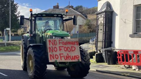 Farmer in tractor with a plaque saying "No farmers, no food, no future"