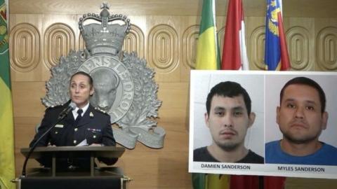 A police officer at press briefing with pictures of murder suspects beside her