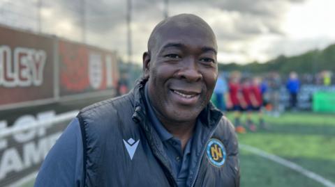 Man smiles at camera, he is wearing a dark jacket and shirt