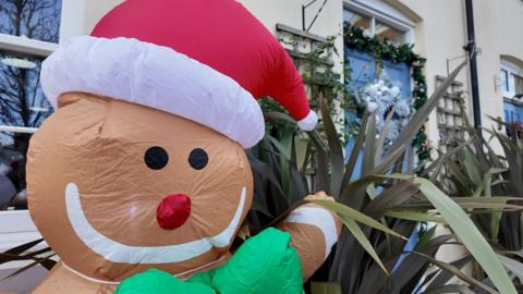 A inflatable gingerbread man outside a house with a white wreath and blue door.
